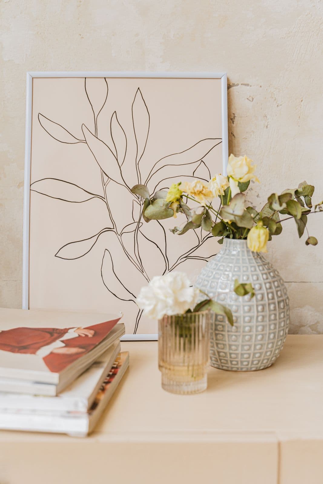 Flores blancas en un jarrón junto a un dibujo de hojas y unos libros